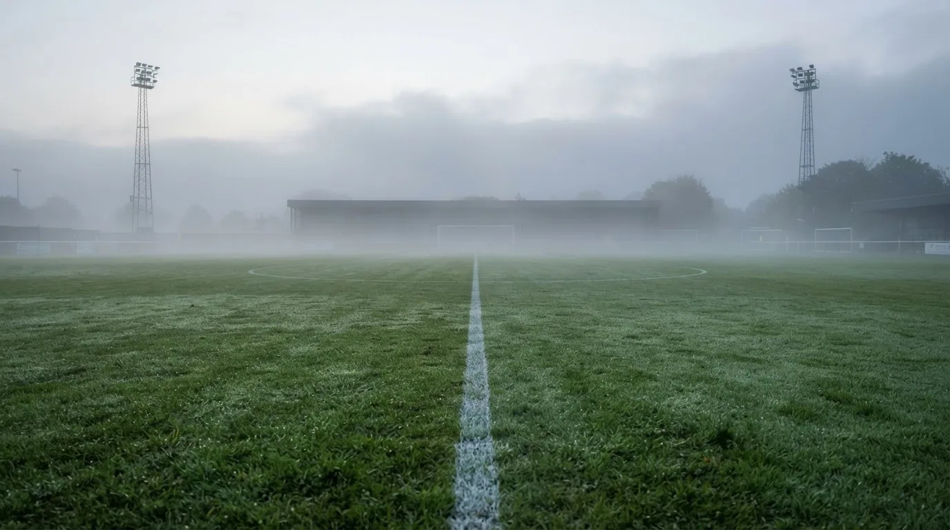 Ein leeres Fußballfeld im Morgennebel, die Mittellinie verliert sich im Dunst, kein Mensch ist zu sehen.