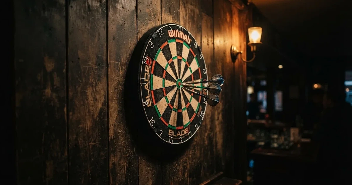 Eine Dartscheibe an einer Holzwand in einem schwach beleuchteten Raum, drei Pfeile stecken nahe der Mitte, warmes Licht von der Seite.
